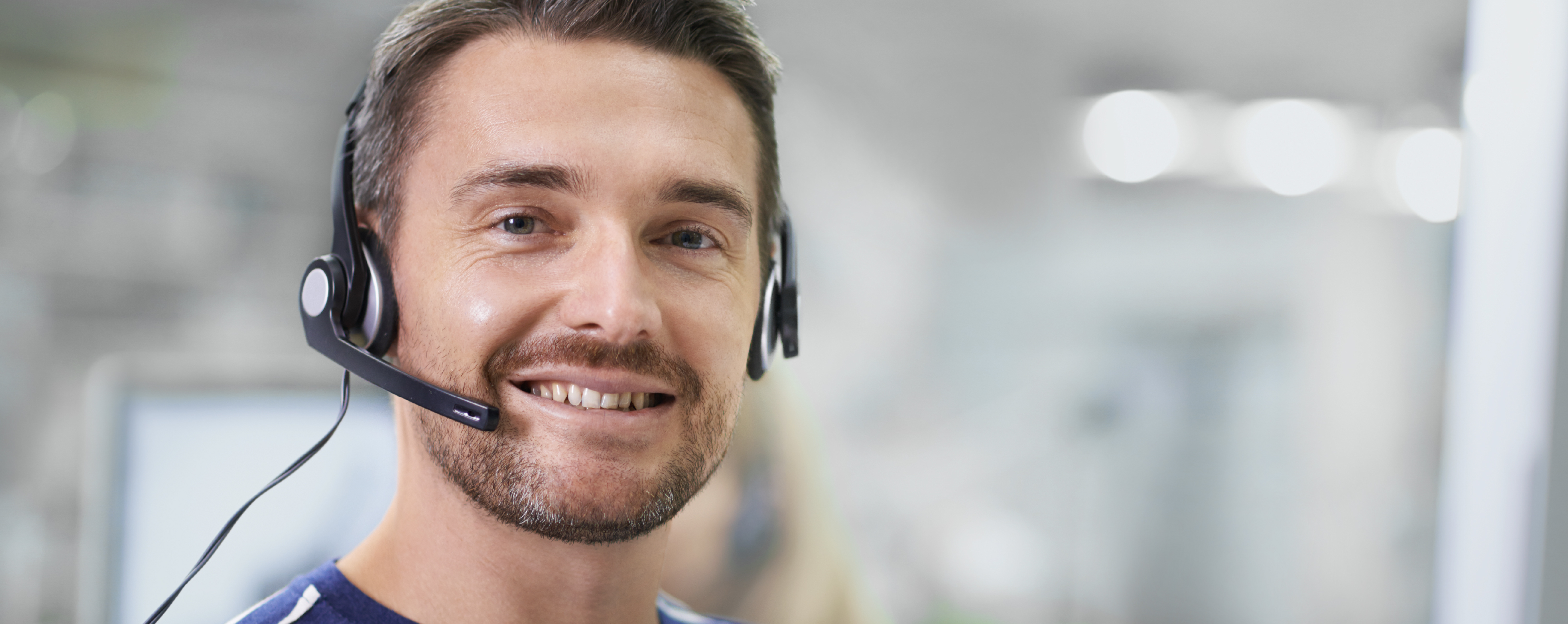 A contact center employee wearing a headset, smiling on a call.