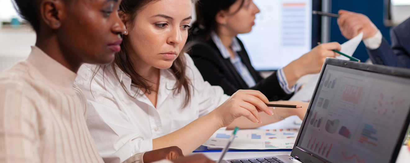 Two business professionals reviewing cost and performance charts on a laptop during a team meeting