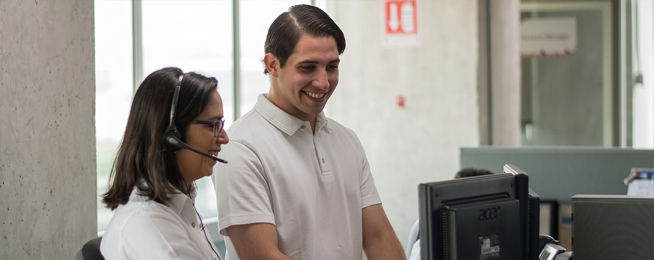 Smiling contact center supervisor coaching an agent wearing a headset as they review her screen together at her desk