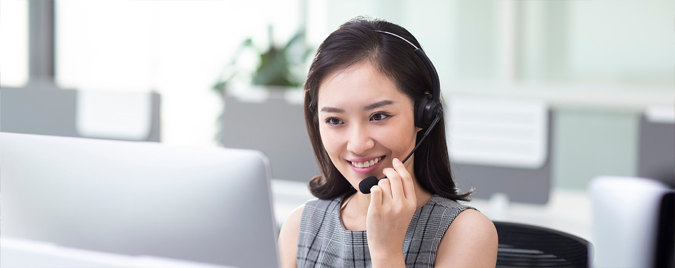 Smiling customer service agent wearing a headset works at a computer in a bright, modern contact center